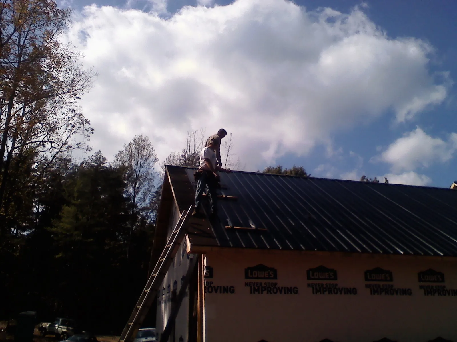 Roofer fastening dark metal panels high against a cloudy sky, from a Roof Inspection job in Mead